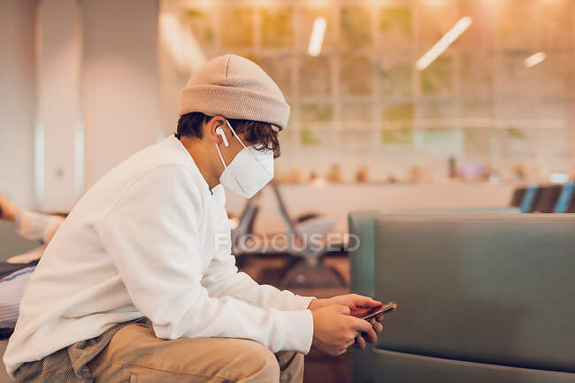 Menino pré-adolescente usando uma máscara usando telefone no aeroporto — Fotografia de Stock