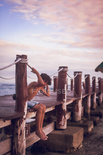 Pre teen boy sitting on a wooden pier at a tropical beach — Stock Photo