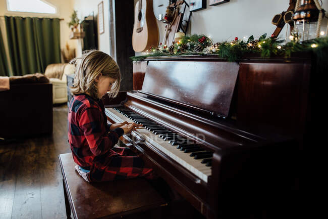 Menino tocando piano com vegetação de Natal — Fotografia de Stock