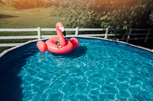 Child on giant flamingo floatie in pool — Stock Photo