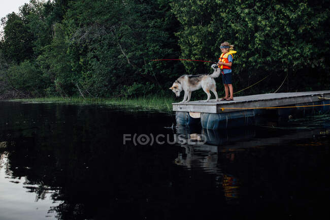Young child fishes on dock with dog — Stock Photo
