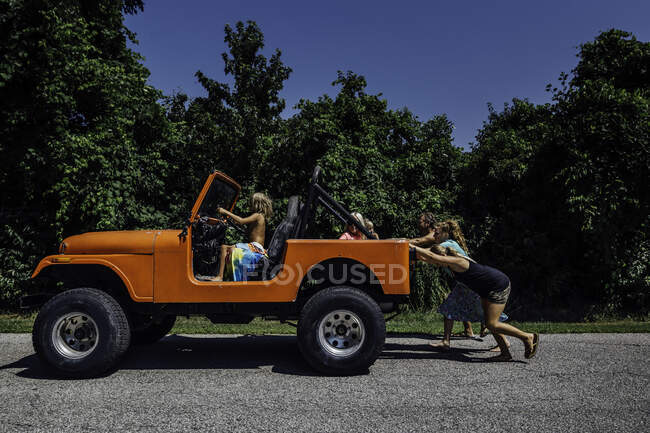 Сім'я штовхає помаранчевий джип, а маленька дитина керує — стокове фото