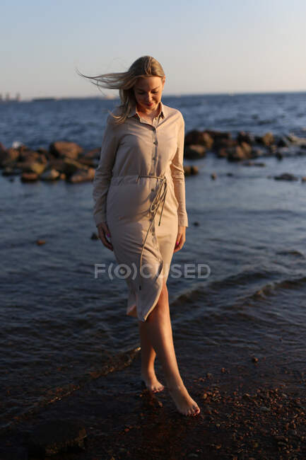 Eine schwangere Frau spaziert im Sommer am Strand entlang. — Stockfoto