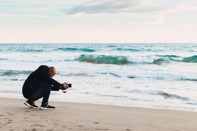 Мужчина фотографирует на пляже на закате — стоковое фото
