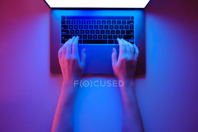 Mãos em um teclado de laptop moderno, vista superior em fundo de néon vermelho e azul brilhante — Fotografia de Stock