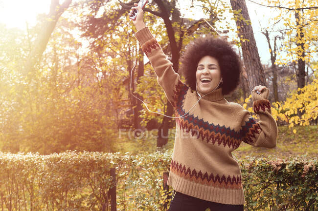 Chica afroamericana paseando disfrutando de la música con sus auriculares en el parque - foto de stock