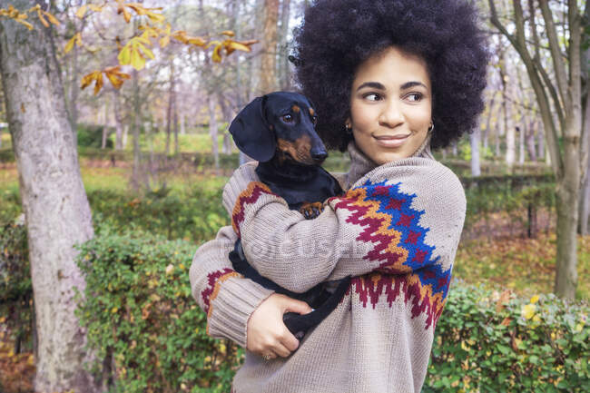 Chica afroamericana sentada y abrazando a su perro en el parque en otoño - foto de stock