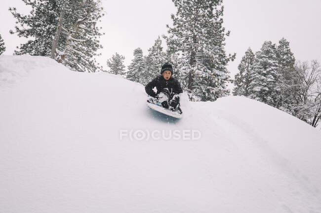 Niño comenzando abajo nevado colina en un trineo - foto de stock