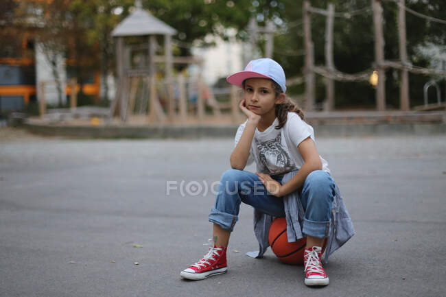 La chica se sienta en una pelota en el patio de recreo. - foto de stock