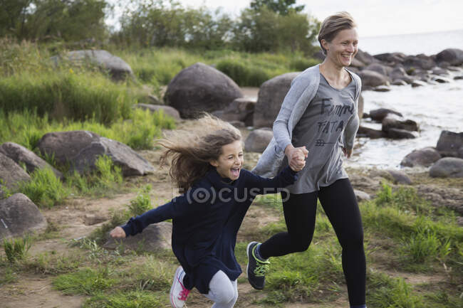 Hija y mamá corren a lo largo de la playa de cerca. - foto de stock