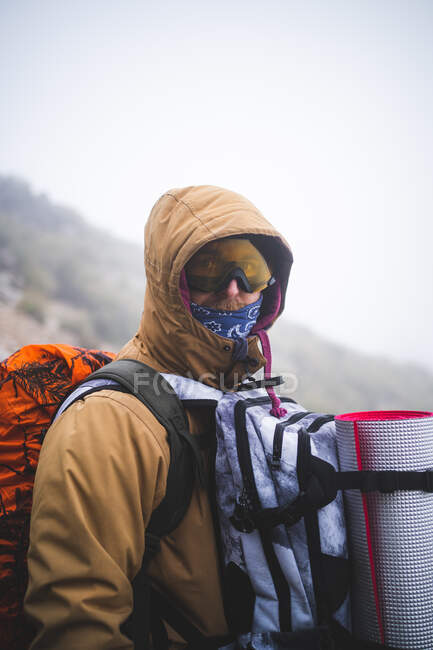 Escursionista in piedi con gli occhiali da sole guardando la fotocamera durante la giornata nebbiosa — Foto stock