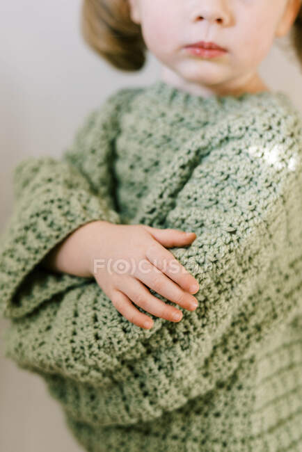 Маленька дівчинка схрещує руки в домашньому зеленому светрі гачком — стокове фото