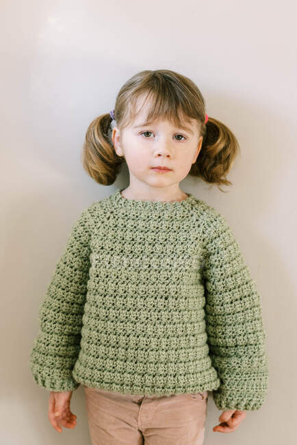 Niño con aspecto neutral en suéter de ganchillo casero y coletas - foto de stock