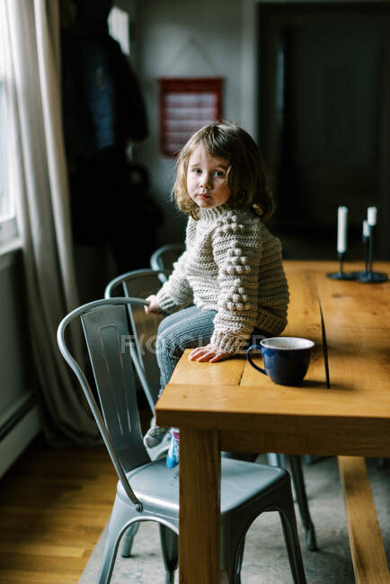 Little girl sitting on table in cozy homemade wool crochet sweater — Stock Photo