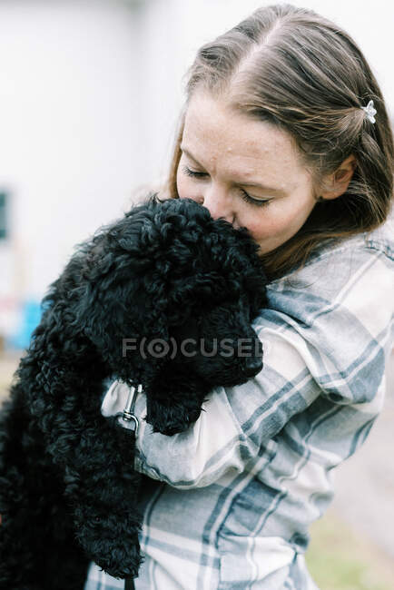 Mulher segurando seu preto novo cachorro poodle bonito nos braços amorosamente — Fotografia de Stock