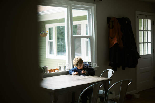 Petit garçon indépendant utilisant sa tablette pour l'école à distance à une table — Photo de stock