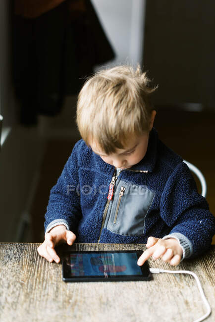 Pequeño niño en la pantalla tiempo jugando juegos en un dispositivo de tableta en casa - foto de stock