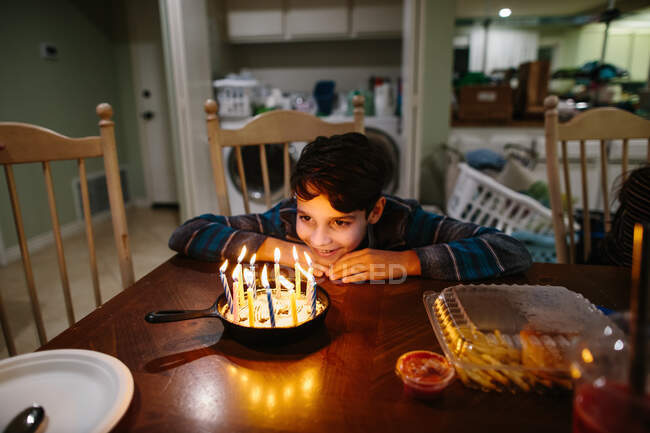 Menino sorri para as velas em seu bolo de aniversário de ferro fundido Pan — Fotografia de Stock
