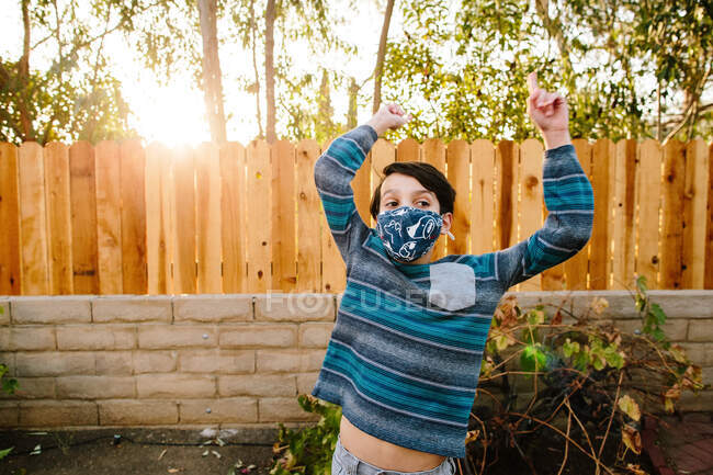 Draußen trägt der Junge eine Gesichtsmaske aus Stoff, hebt die Arme nach oben und legt den Bauch frei — Stockfoto