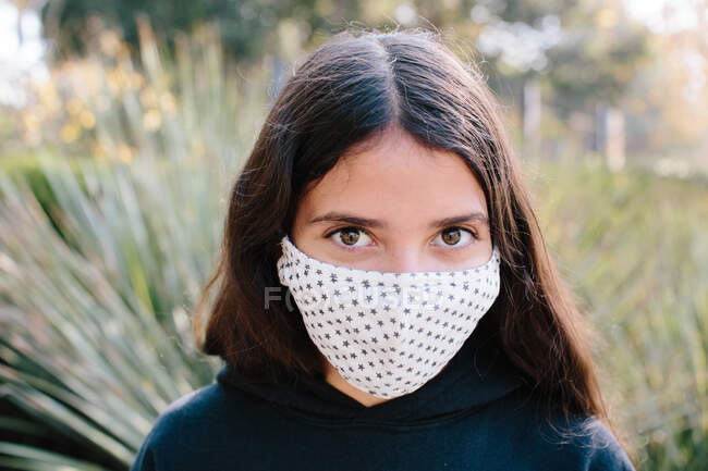 Між дівчиною дивлячись на камеру під час одягу тканини маски для обличчя — стокове фото
