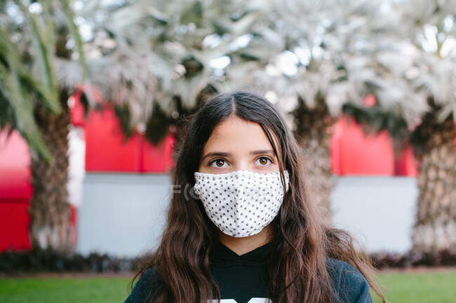 Tween menina vestindo uma máscara de rosto de pano fora olhando lá fora — Fotografia de Stock
