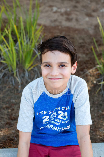 Schulalter Junge, der draußen sitzt, bietet ein unheimliches Lächeln mit geschlossenem Mund — Stockfoto