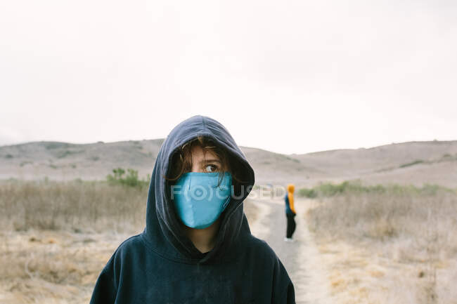 Teenie-Mädchen mit Kapuzenpulli und blauer Gesichtsmaske steht auf einem Naturpfad — Stockfoto