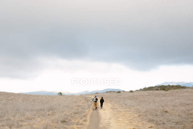 Sous un ciel nuageux vu de derrière un père et une fille en randonnée — Photo de stock