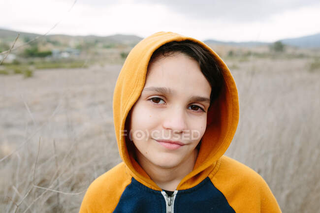 Retrato de um menino vestindo um capuz laranja fora na natureza — Fotografia de Stock