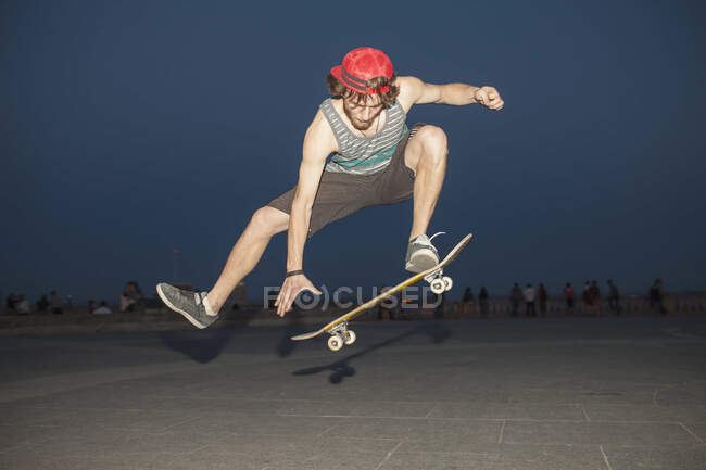 Young skateboard enthusiast flpping his board at night — Stock Photo