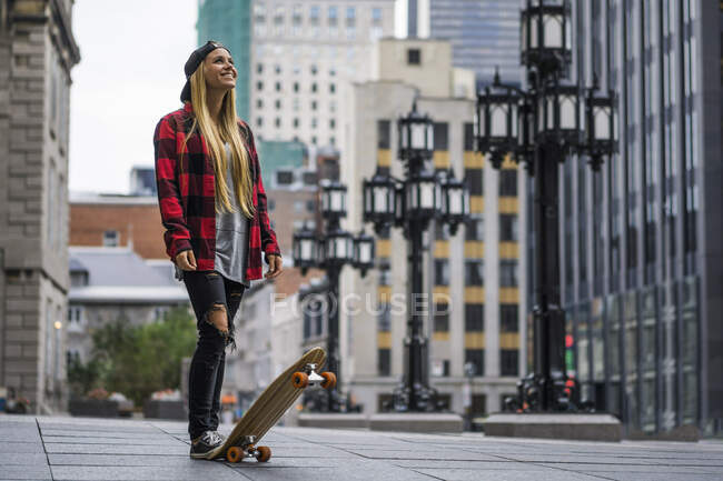 Stylish female millennial in urban area with skateboard looking upwards happily, Montreal, Quebec, Canada — Stock Photo