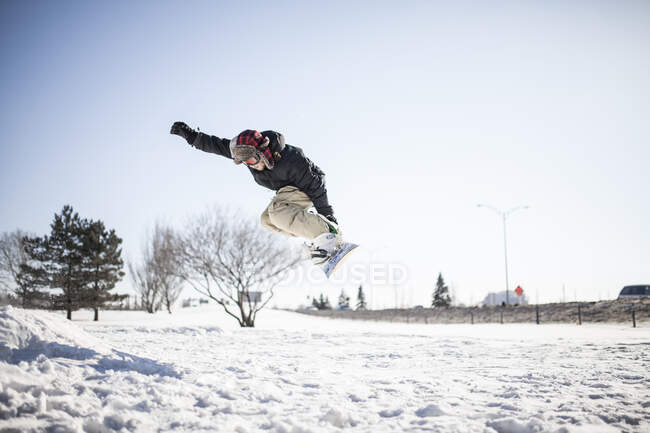 Jeune homme en snowboard effectuant une cascade en plein air — Photo de stock