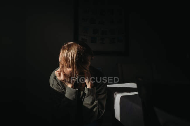 Adult woman looking distressed with face in hand with dark backdrop — Stock Photo