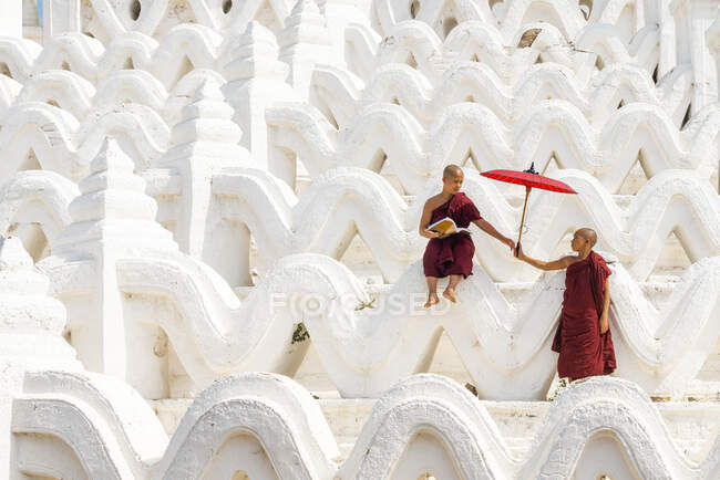 Новичок-монах, дающий зонтик другому послушнику пагоды Синбюме, Мингун, Мандалай, поселок Сагаин, район Сагаин, регион Сагаин, Мьянма — стоковое фото