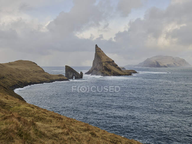 Formaciones rocosas Drangarnir y Tindhlmur en la distancia en las Islas Feroe - foto de stock