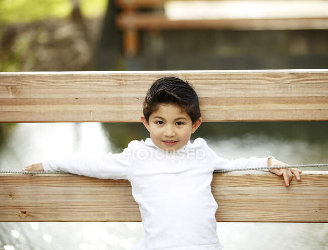 Мальчик смотрит в камеру на мосту в парке — стоковое фото