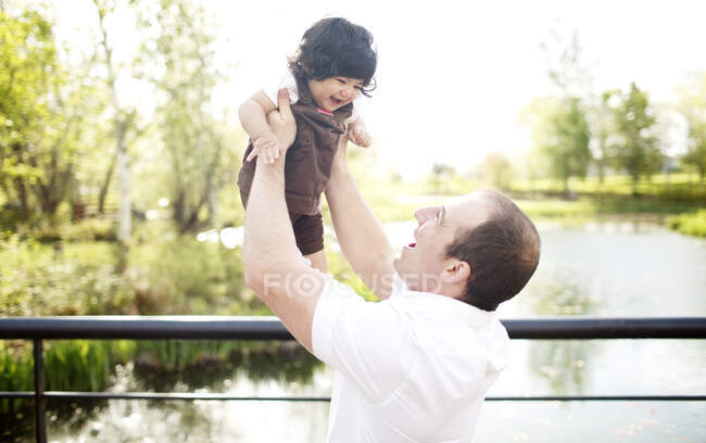 Pai segurando filha no ar na ponte do parque — Fotografia de Stock