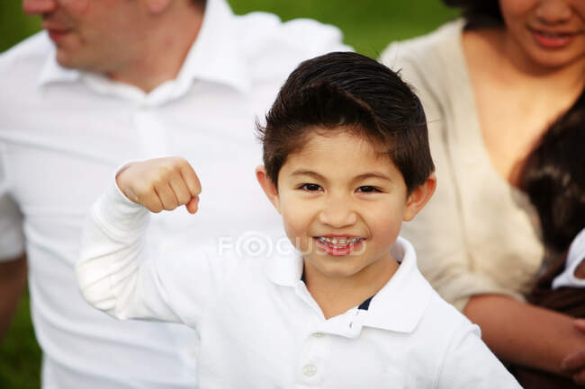 Niño flexing mientras sentado en frente de la familia en hierba - foto de stock