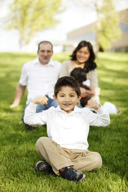 Мальчик сгибается, сидя перед семьей в траве — стоковое фото