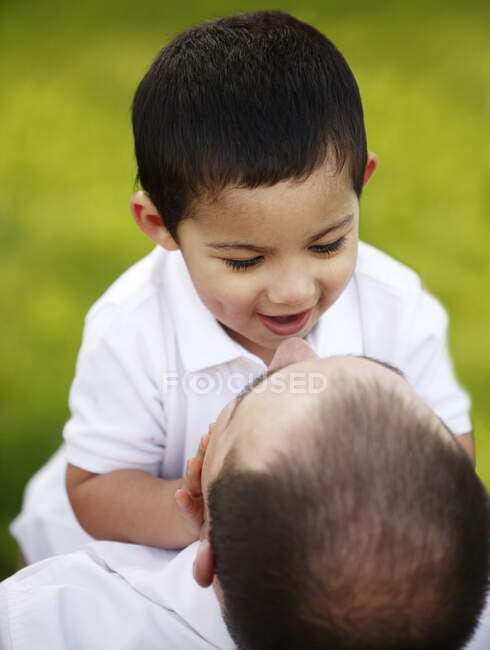 Closeup of father holding up toddler son in park — Stock Photo