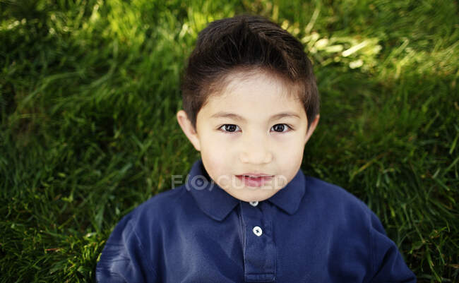 Young boy laying in grass looking up at camera — Stock Photo