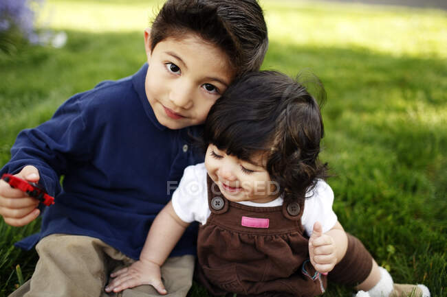 Joven y su hermana pequeña mirando a la cámara, en el parque - foto de stock