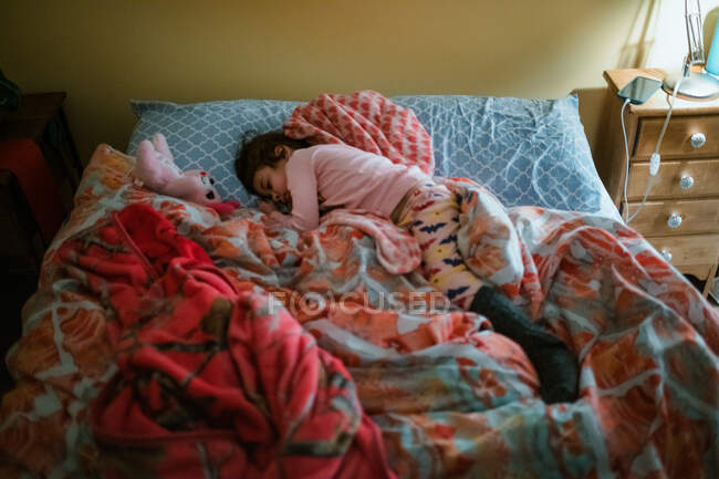 Niña de raza mixta durmiendo en la cama con edredón rosa - foto de stock