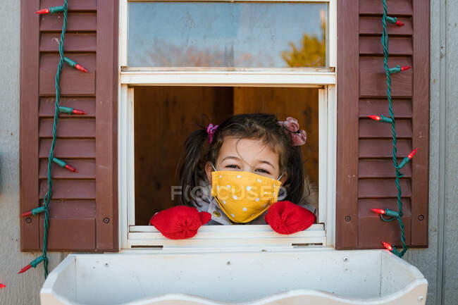 Young girl looking through window with face mask Christmas lights — Stock Photo