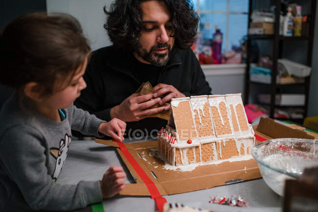 Padre e figlia che costruiscono casa di pan di zenzero al tavolo della cucina — Foto stock