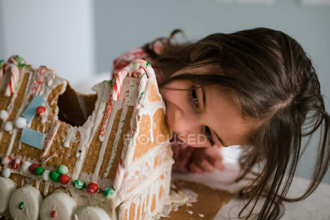 Young female child eating gingerbread house big bite — Stock Photo