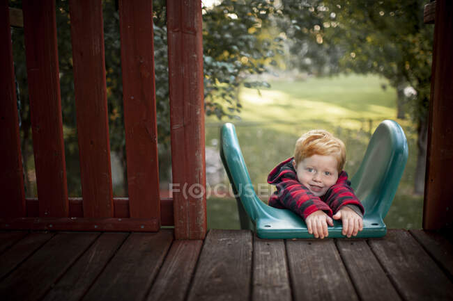 Toddler boy 3-4 years old holding on to top of slide on stomach — Stock Photo