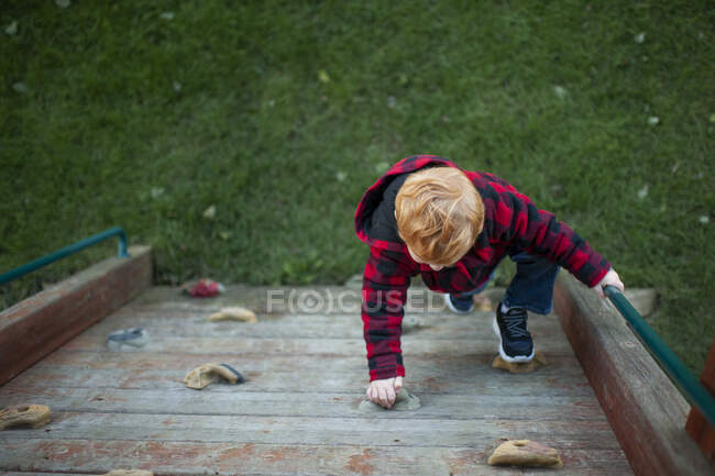 Above view of toddler boy climbing rock wall outdoors in winter coat — Stock Photo