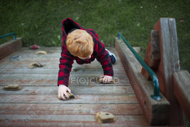 Birds eye view of toddler climbing rock wall on playset in fall coat — Stock Photo