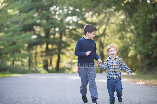 Two brothers running down a road while hands smiling — Stock Photo